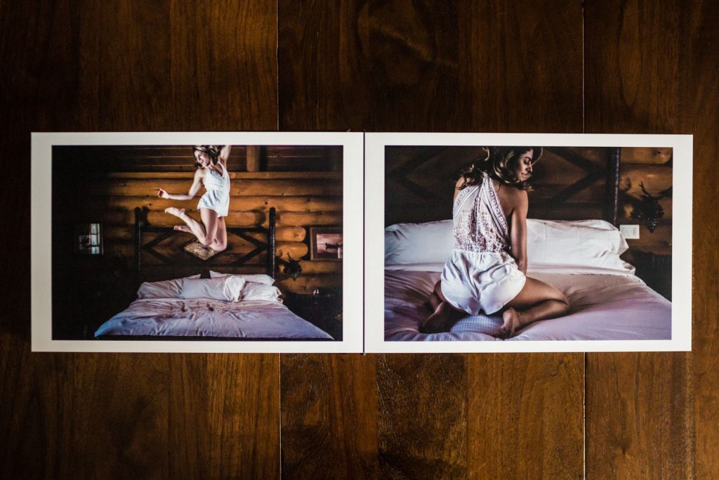 Two printed photos on a wooden surface: the left shows a woman jumping on a bed, the right shows her kneeling on the bed, both in a cozy, dimly lit room with wood-paneled walls.