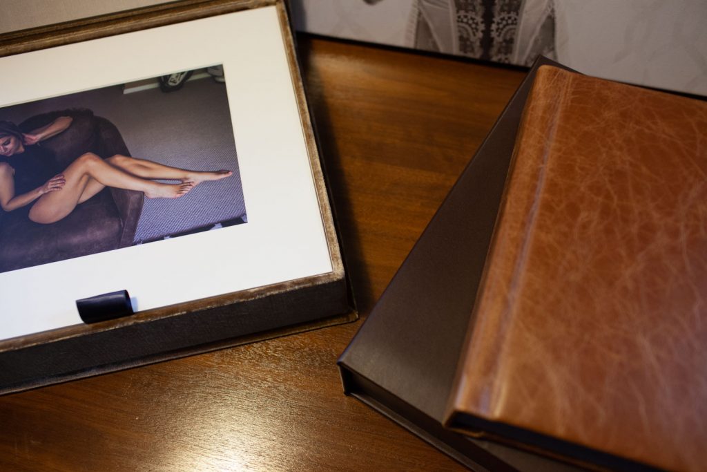 A matted photograph of a woman lounging on a couch is displayed in an open box next to two closed leather-bound photo albums on a wooden surface.