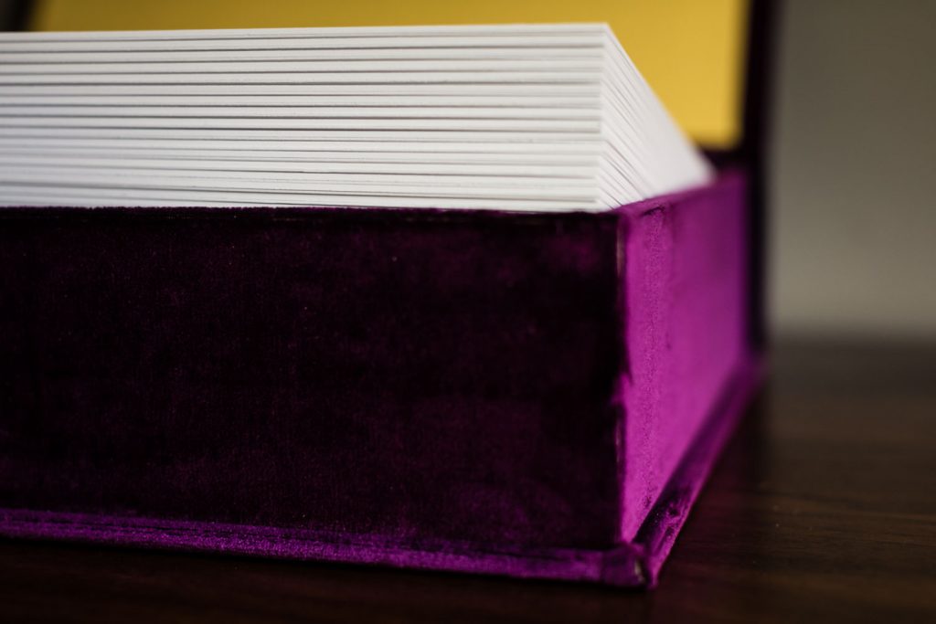 A close-up of a stack of white papers inside a purple velvet box with a yellow interior, set on a dark wooden surface.