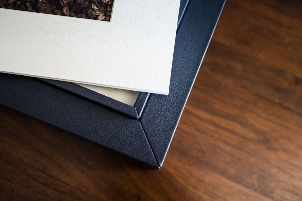 A close-up of a photo mat with a printed image on top of a dark blue leather-bound photo album, both resting on a wooden surface.