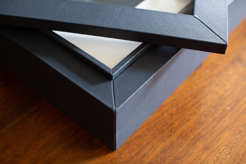 Close-up of the corners of two black picture frames, one resting on top of the other, placed on a wooden surface.