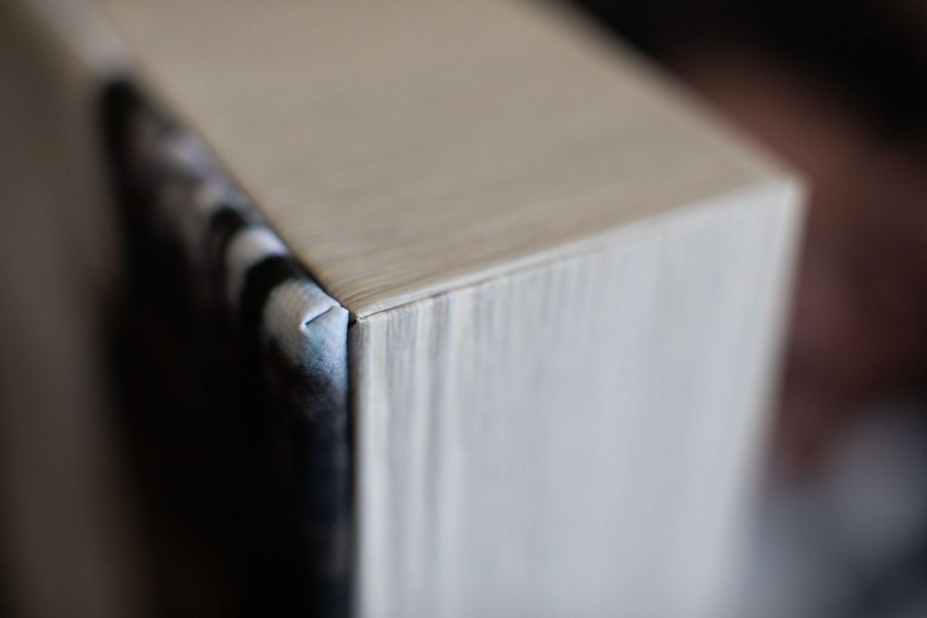 Close-up of the top corner of a thick, closed book, showing the pages and the edge of the cover with a small fold in the dust jacket. The background is blurred.