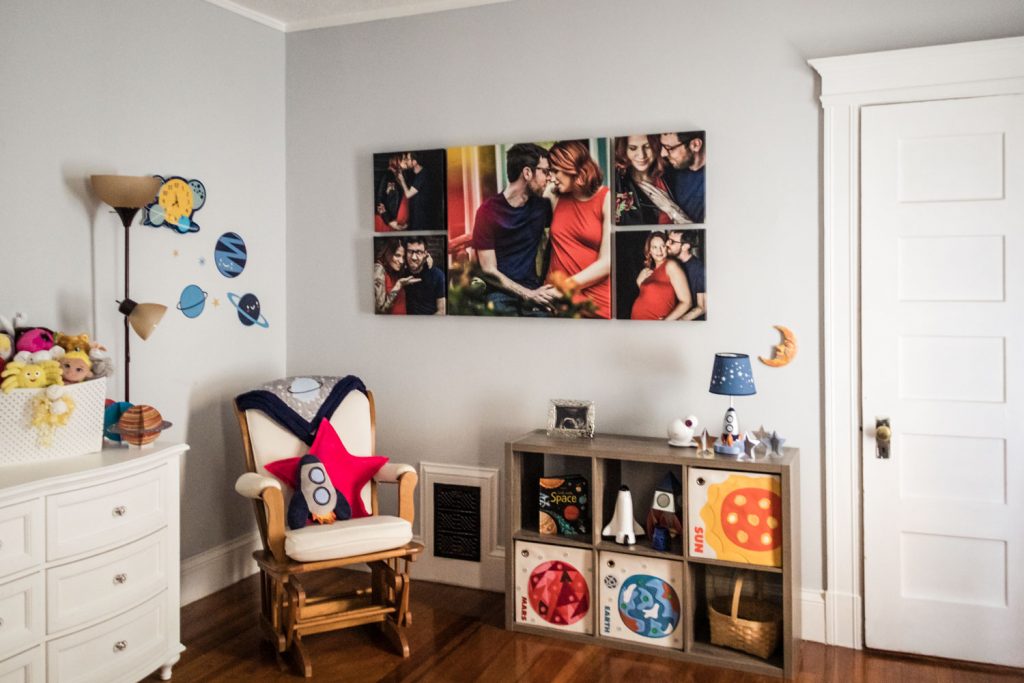A cozy childrens room with a rocking chair, plush toys, space-themed decorations, a white dresser, and a wall featuring a collage of family photos above a shelf with books and toy rockets.