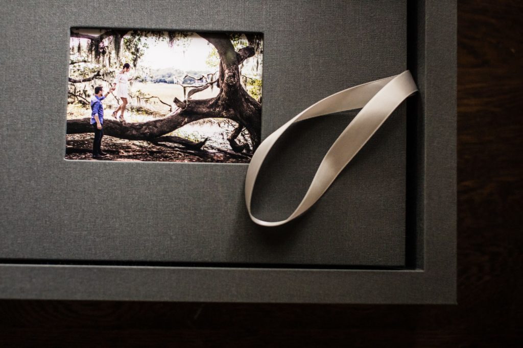 A gray textured box with a white ribbon and a small photo inset showing children playing on a large tree branch outdoors.