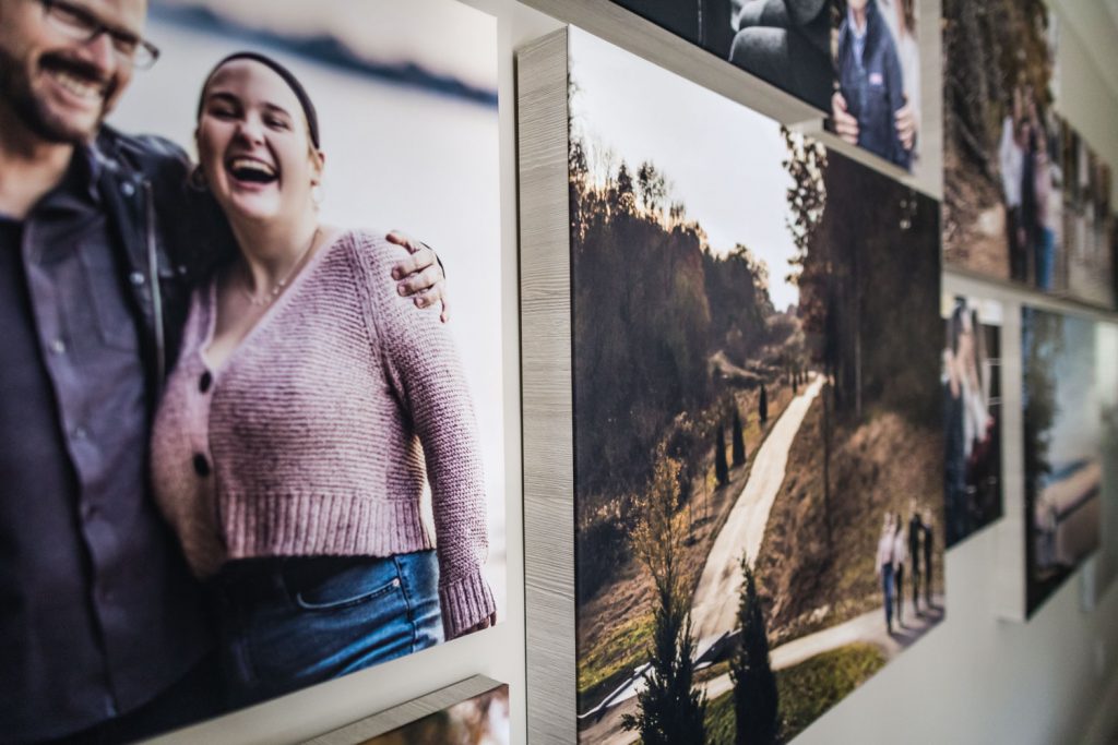 A close-up of a gallery wall featuring canvas prints, including a smiling couple in the foreground and outdoor landscape photos with paths and trees in the background.