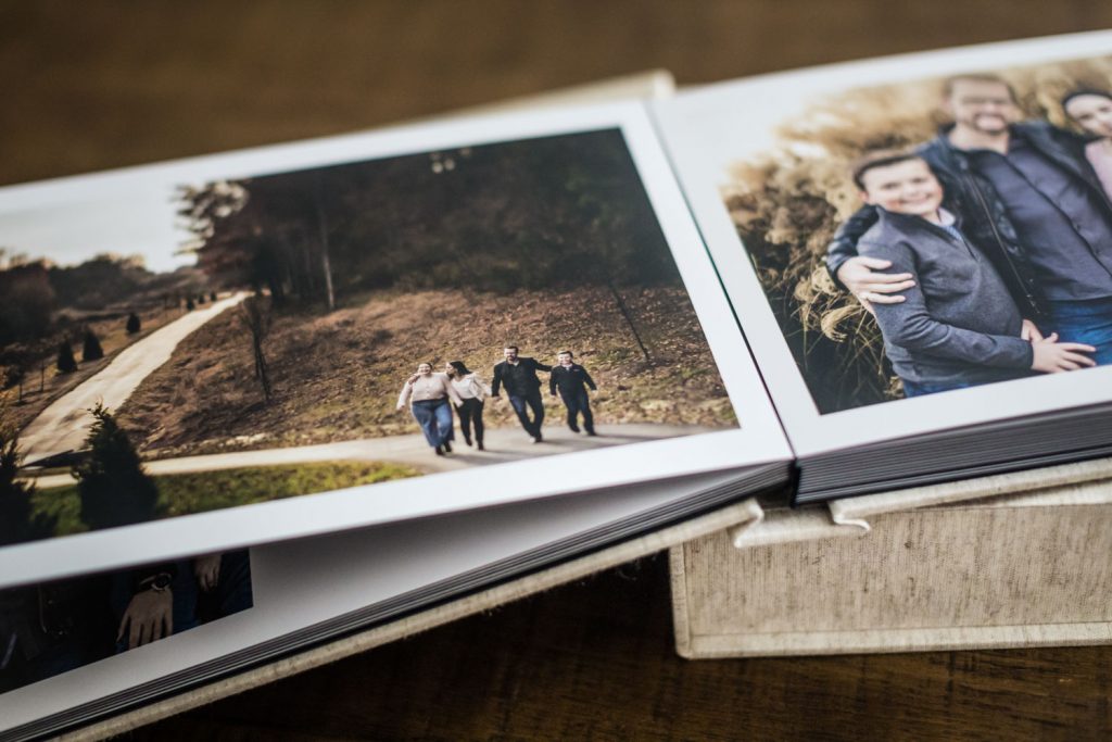 A close-up of an open photo album showing two family photos, one of a group walking outdoors on a path and another of people smiling and embracing, with a wooden table in the background.