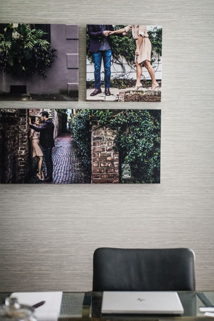 A desk with a closed HP laptop and pen sits below a wall decorated with two romantic photos of a couple and one photo of greenery on a building.