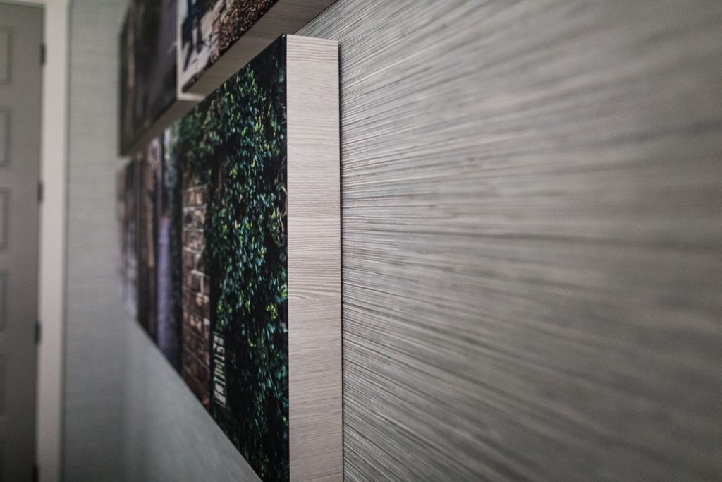 Close-up side view of canvases hanging on a textured, light-colored wall, showing the thick edges of the prints and part of a door in the background.