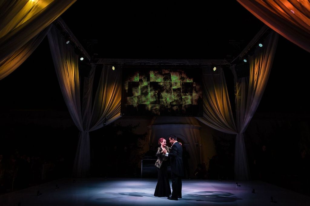 Artistic Composition A couple in formal attire dances together on a dimly lit stage, surrounded by draped curtains and illuminated by soft spotlights, creating an elegant and intimate atmosphere.